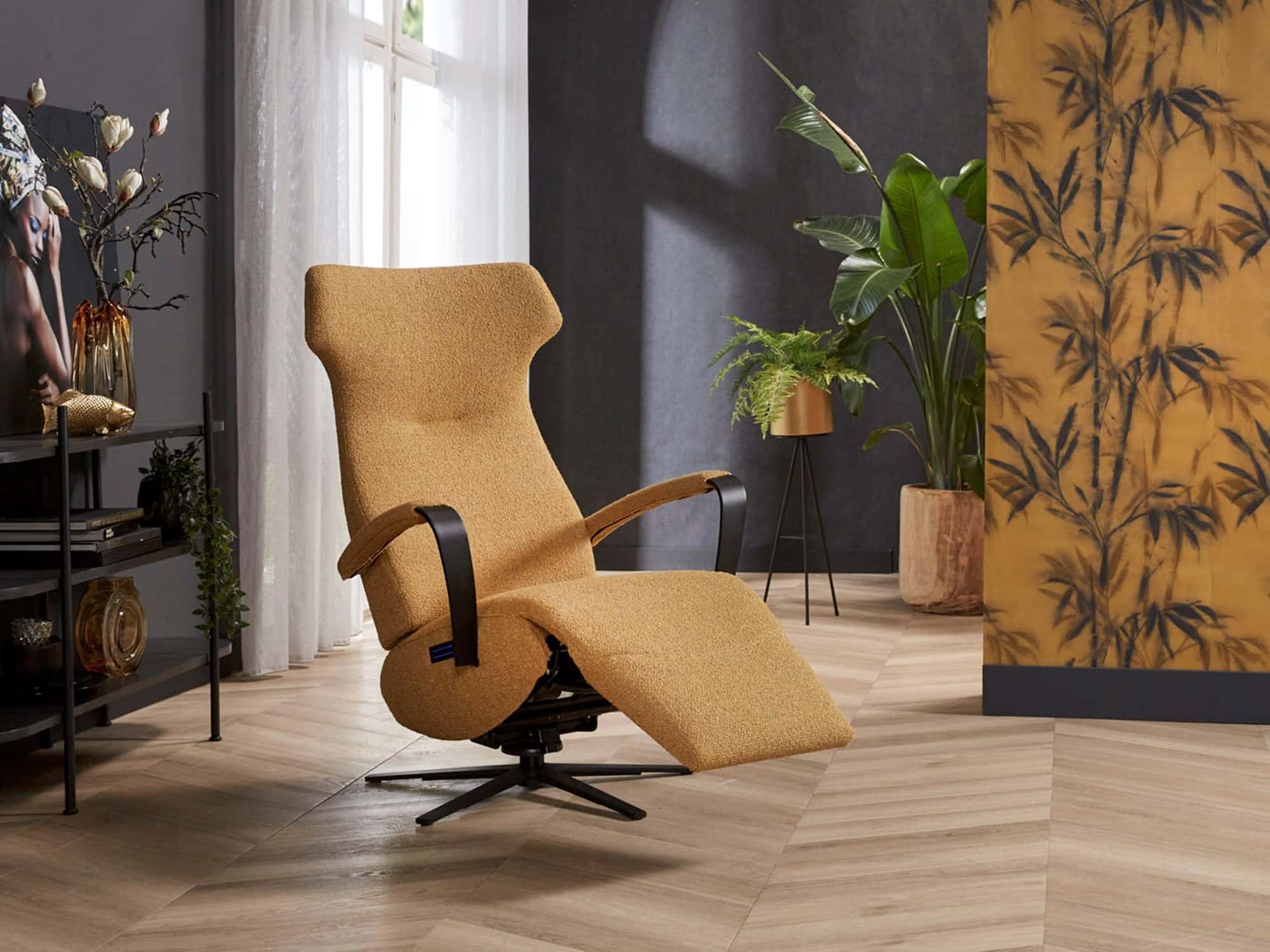 Mosterdgele relaxfauteuil met zwarte armleuningen en planten in achtergrond